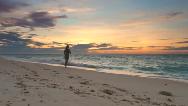 Joven mujer corre de la costa del océano puesta de sol fondo — Vídeo de stock