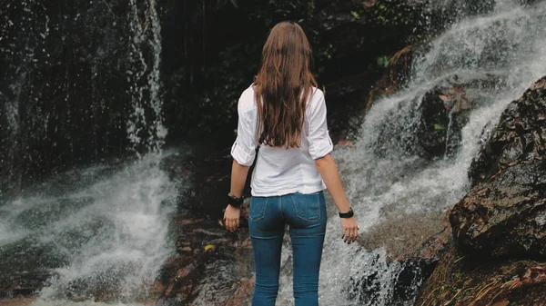 Turista mujer levantar las manos a salpicaduras cascada —  Fotos de Stock