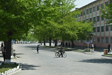Kaesong, Kuzey Kore - 5 Mayıs 2019: Şehir sokakları. Şehir hayatı. İnsanlar şehir sokaklarında kendi işlerinde bisikletle gezerler.