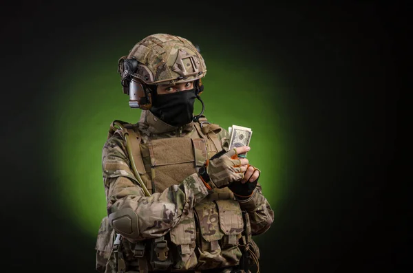 A male soldier in military clothes with a weapon on a dark background with money — Stock Photo, Image