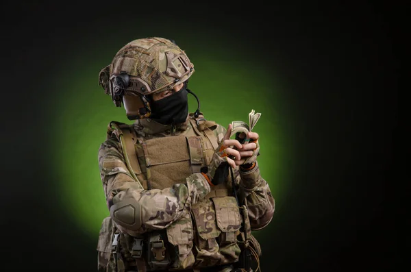 A male soldier in military clothes with a weapon on a dark background with money — Stock Photo, Image