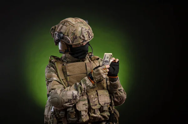 En manlig soldat i militära kläder med ett vapen på en mörk bakgrund med pengar — Stockfoto