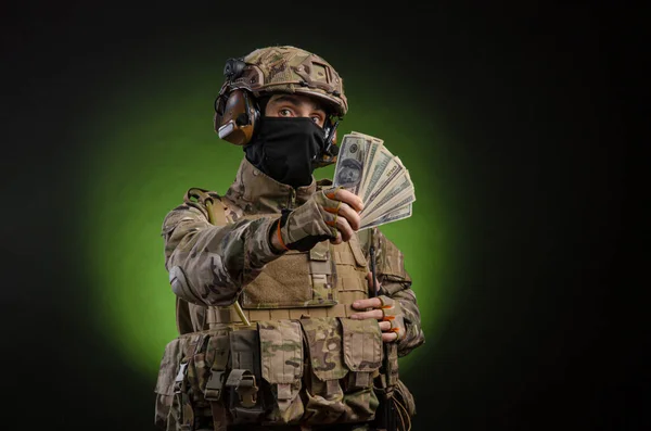 A male soldier in military clothes with a weapon on a dark background with money — Stock Photo, Image