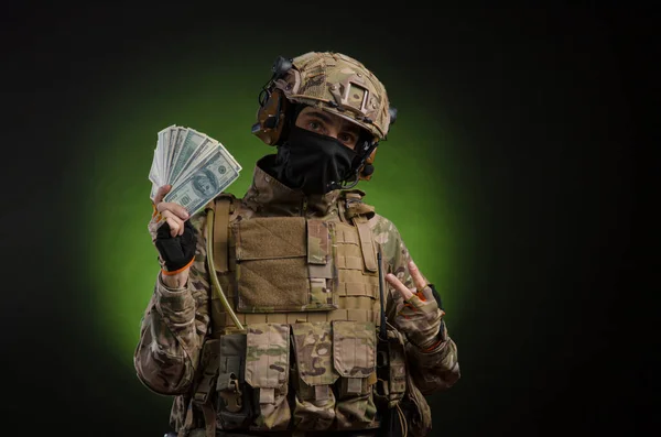 Um soldado masculino em roupas militares com uma arma em um fundo escuro com dinheiro — Fotografia de Stock