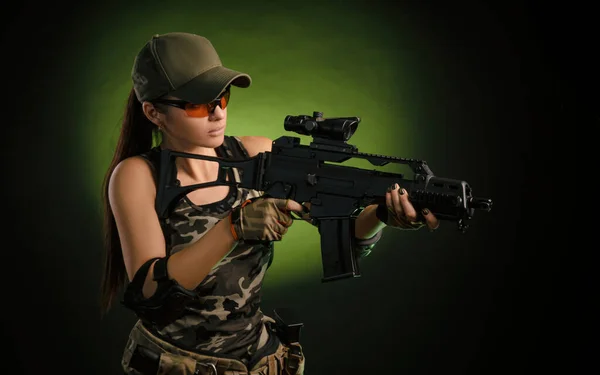 The girl in military overalls airsoft posing with a gun in his hands on a dark background in the haze — Stock Photo, Image