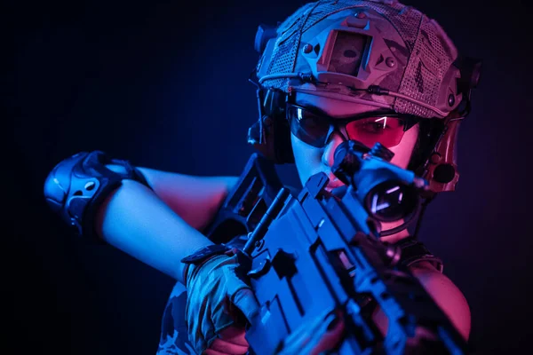 Dziewczyna w wojskowych kombinezonach airsoft pozowanie z pistoletem w rękach na ciemnym tle w mgle w neonowym świetle — Zdjęcie stockowe