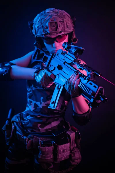 Dívka ve vojenských kombinézách airsoft pózuje s pistolí v rukou na tmavém pozadí v oparu v neonovém světle — Stock fotografie