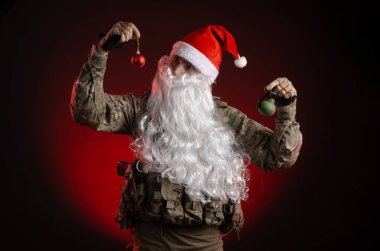 Silahlı ve Noel Baba şapkalı askeri üniformalı bir adam.