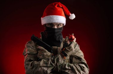 Silahlı ve Noel Baba şapkalı askeri üniformalı bir adam.