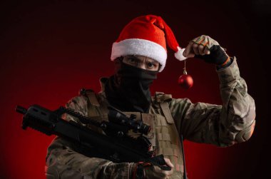Silahlı ve Noel Baba şapkalı askeri üniformalı bir adam.