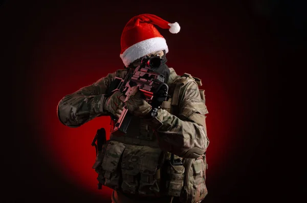 A man in a military uniform with a gun and a Santa Claus hat — Stock Photo, Image