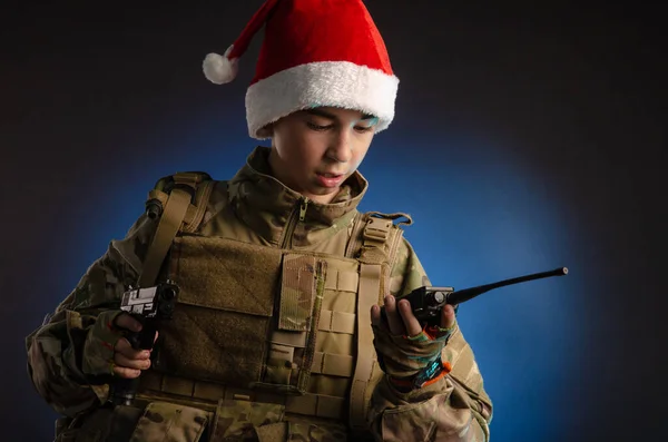 A teenager in a soldiers uniform and Santa Claus hat is talking on the radio — Stock Photo, Image