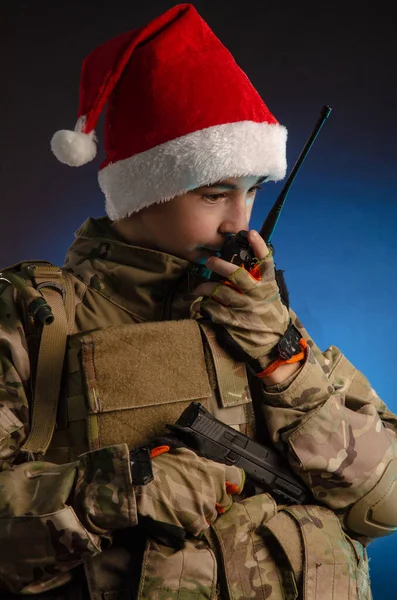 A teenager in a soldiers uniform and Santa Claus hat is talking on the radio — Stock Photo, Image