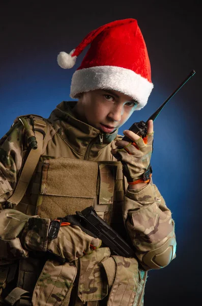 A teenager in a soldiers uniform and Santa Claus hat is talking on the radio — Stock Photo, Image
