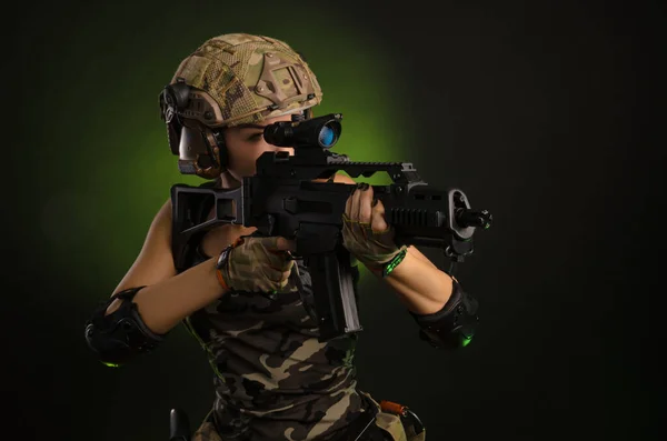 The girl in military overalls airsoft posing with a gun in his hands on a dark background in the haze — Stock Photo, Image