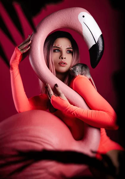 Uma menina em um bodysuit brilhante com uma grande figura Flamingo e um rato vivo — Fotografia de Stock