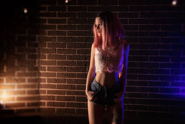 一个身材苗条的女孩靠着砖墙，穿着短裤，背带着毒液灯 — 图库照片