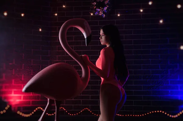 Uma menina em um bodysuit brilhante posa com uma grande estatueta Flamingo — Fotografia de Stock
