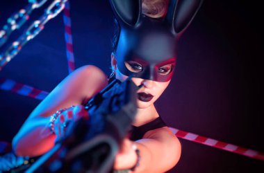 Deri elbiseli ve elinde silah olan siyah tavşan maskeli bir kadın.