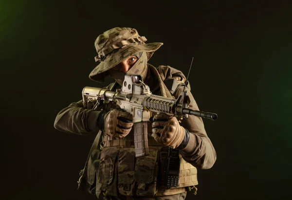 Солдат-табуретка у військовому одязі зі зброєю на темному тлі — стокове фото