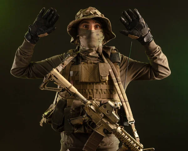 Sabotér voják ve vojenském oblečení se zbraní na tmavém pozadí se vzdává s rukama nad hlavou — Stock fotografie
