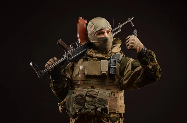 Sabotér voják ve vojenském oblečení se zbraní na tmavém pozadí ukazuje gesta — Stock fotografie