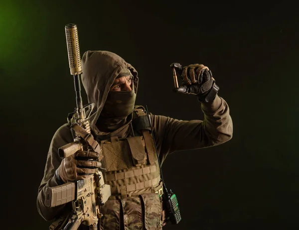 Um soldado-sabotador de uniforme militar com uma arma no fundo escuro mostra uma bala — Fotografia de Stock
