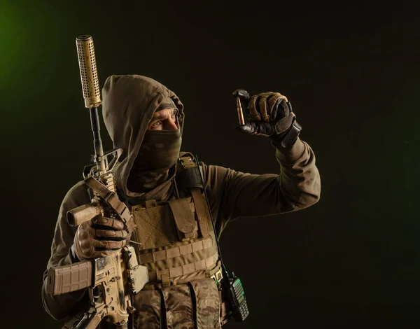 A soldier-saboteur in military uniform with a weapon on a dark background shows a bullet — Zdjęcie stockowe