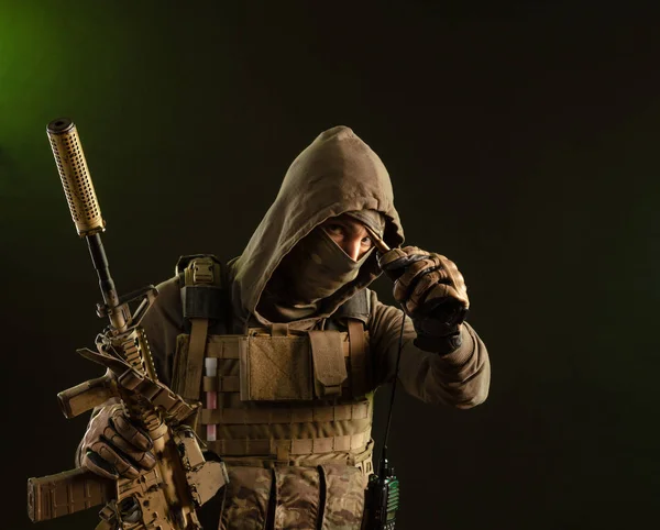 A soldier-saboteur in military uniform with a weapon on a dark background shows a bullet — Stockfoto