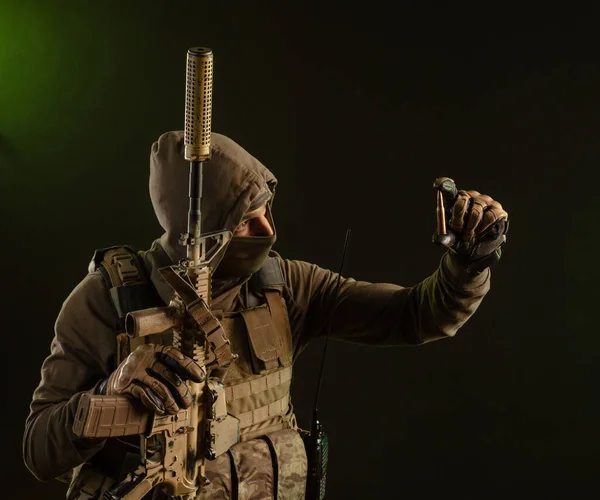 A soldier-saboteur in military uniform with a weapon on a dark background shows a bullet — 스톡 사진