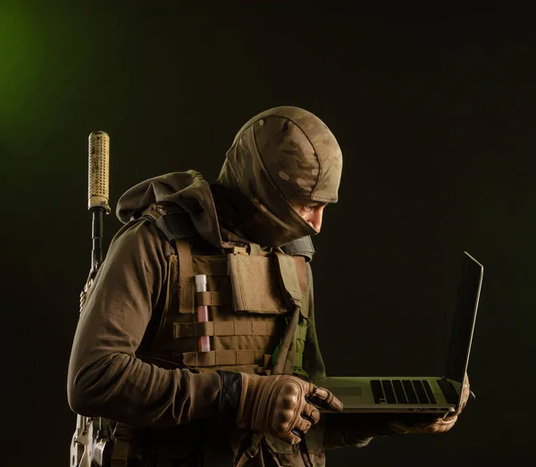 Saboteur soldier in military clothing with a weapon on a dark background with a laptop — Stock Photo, Image