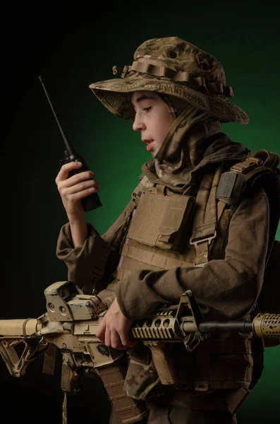 A boy in military uniform with a rifle speaking from radio — Stock Photo, Image
