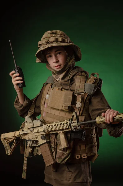 Um rapaz de uniforme militar com uma espingarda a falar pelo rádio — Fotografia de Stock