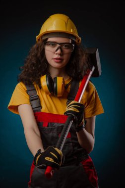 the girl in the construction helmet and overalls with a sledgehammer