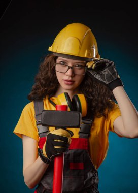 the girl in the construction helmet and overalls with a sledgehammer