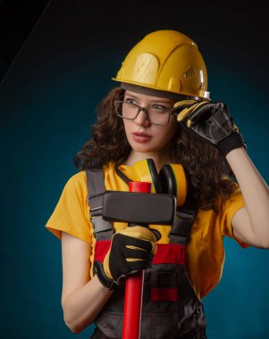 the girl in the construction helmet and overalls with a sledgehammer