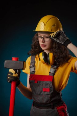 the girl in the construction helmet and overalls with a sledgehammer