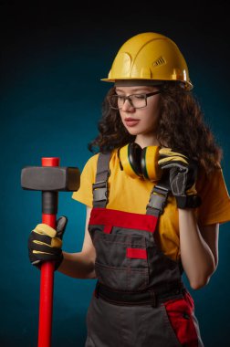 the girl in the construction helmet and overalls with a sledgehammer