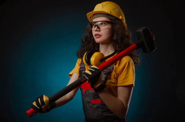 the girl in the construction helmet and overalls with a sledgehammer