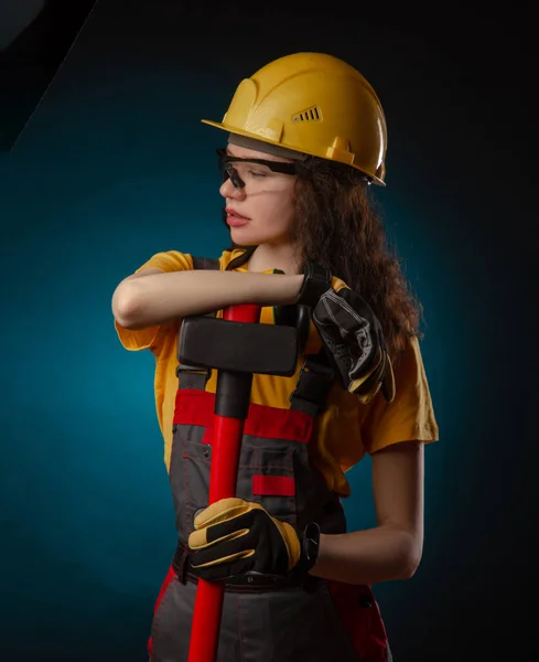 The girl in the construction helmet and overalls with a sledgehammer — Stockfoto