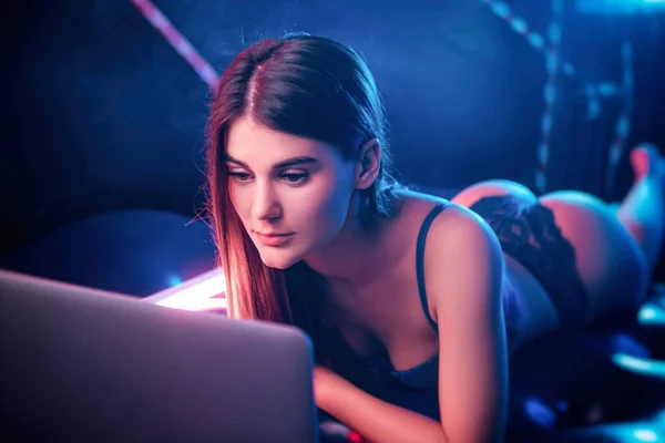 beautiful girl in neon light with laptop lying