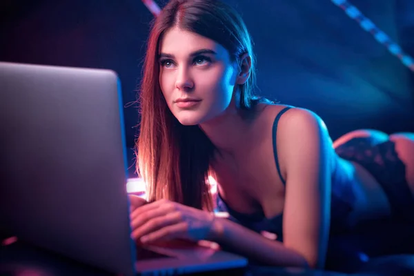Beautiful girl in neon light with laptop lying — 스톡 사진