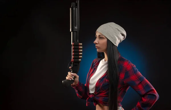 La ragazza in camicia a quadri su uno sfondo scuro con un fucile da caccia — Foto Stock