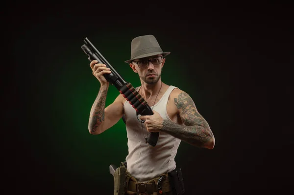 Athletic guy with a tattoo poses with a shotgun — Stock Photo, Image