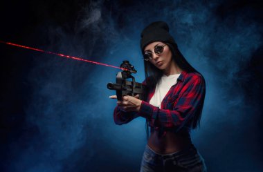 Siyah arka planda, otomatik tüfekli, kareli tişörtlü bir kız.