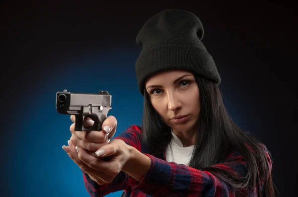 En flicka i en incheckad skjorta på en mörk bakgrund med en pistol — Stockfoto