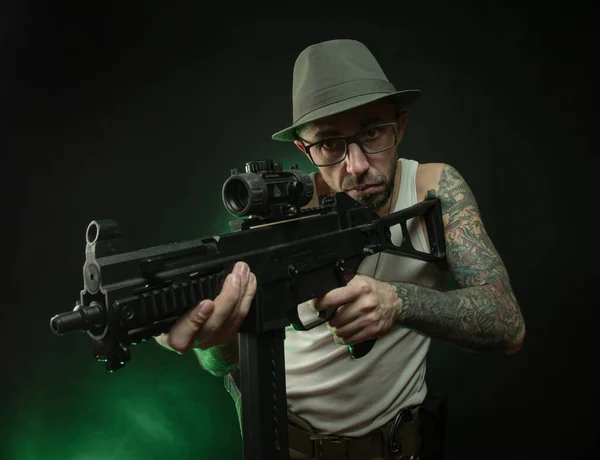 A sporty guy with a tattoo poses with an automatic rifle — Stock Photo, Image