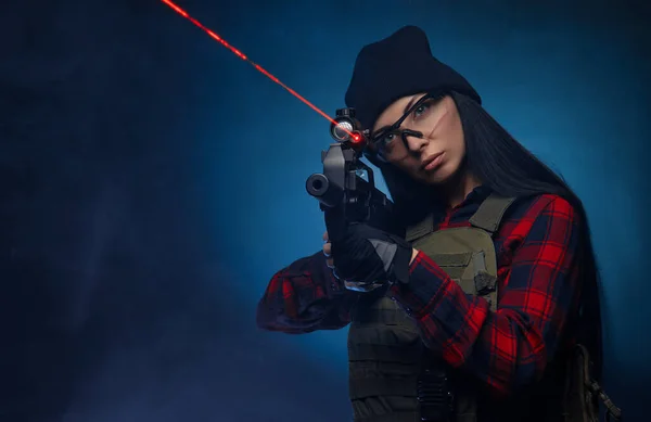 Ein Mädchen im karierten Hemd vor dunklem Hintergrund mit einem automatischen Gewehr — Stockfoto