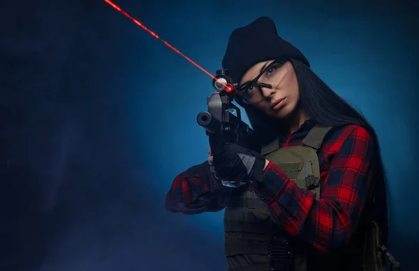 Una chica con camisa a cuadros sobre un fondo oscuro con un rifle automático — Foto de Stock