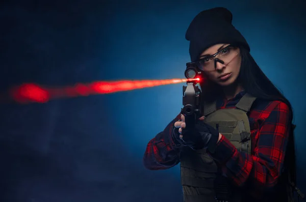 Una chica con camisa a cuadros sobre un fondo oscuro con un rifle automático — Foto de Stock